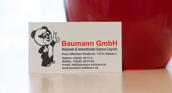 weisse-Visitenkarte-der-Firma-Baumann-mit-roter-und-schwarzer-Schrift-und-Panda-Logo